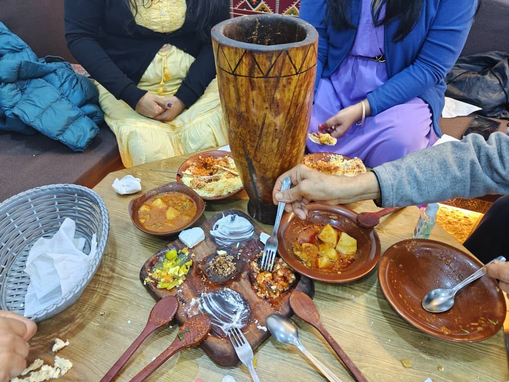 Hands reaching into a spread of stews, salads and bread on a shared table