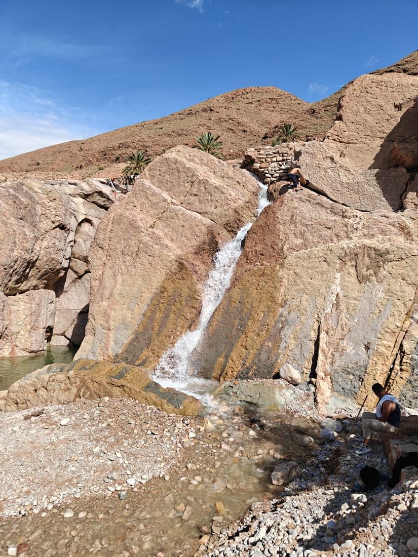 A small waterfall pouring between tilted rock slabs in a desert gorge