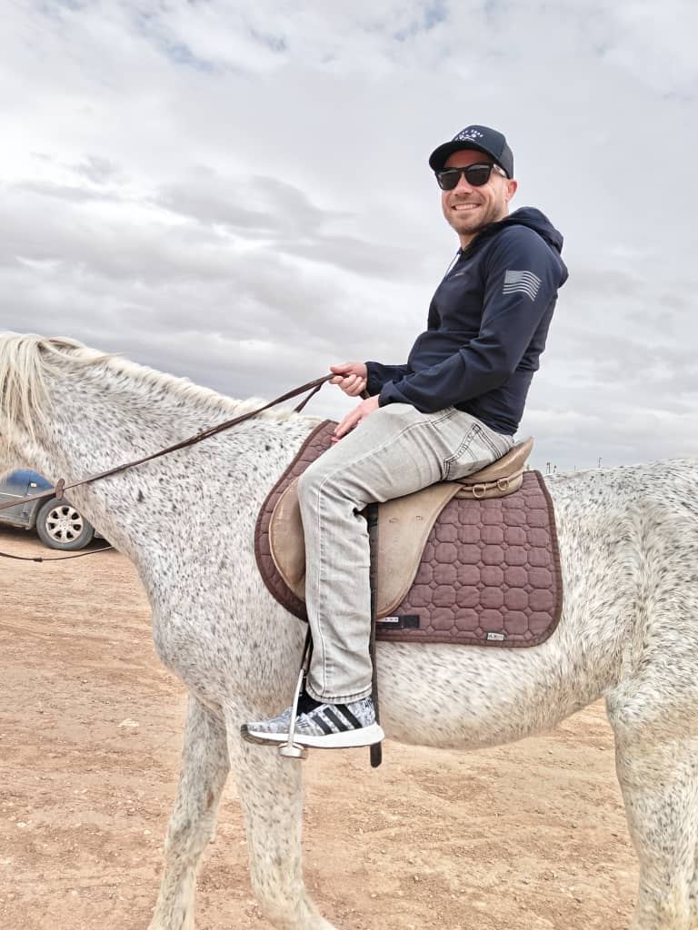 A traveller riding a grey horse on a sandy track