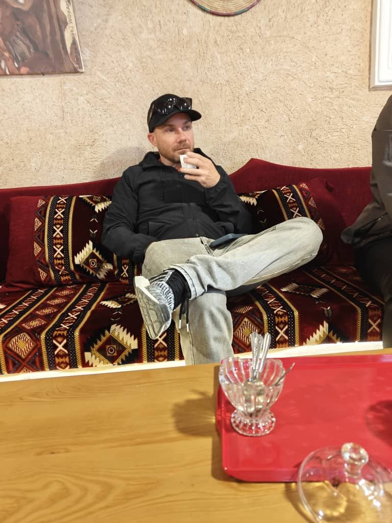 A traveller drinking tea on a red patterned banquette in a guesthouse sitting room