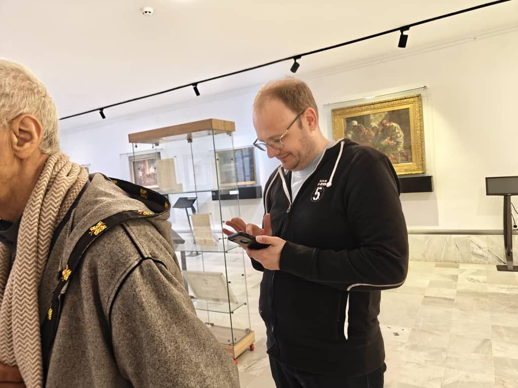Visitors reading the labels in a museum gallery of glass cases and framed paintings
