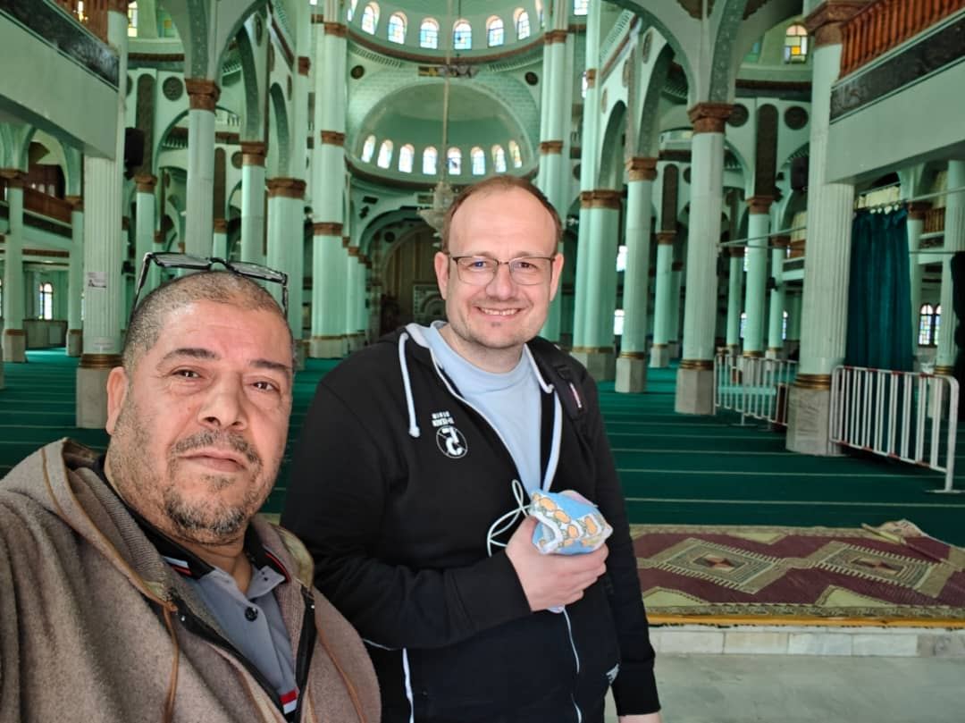 A local guide and a traveller taking a selfie inside a pale green, pillared mosque