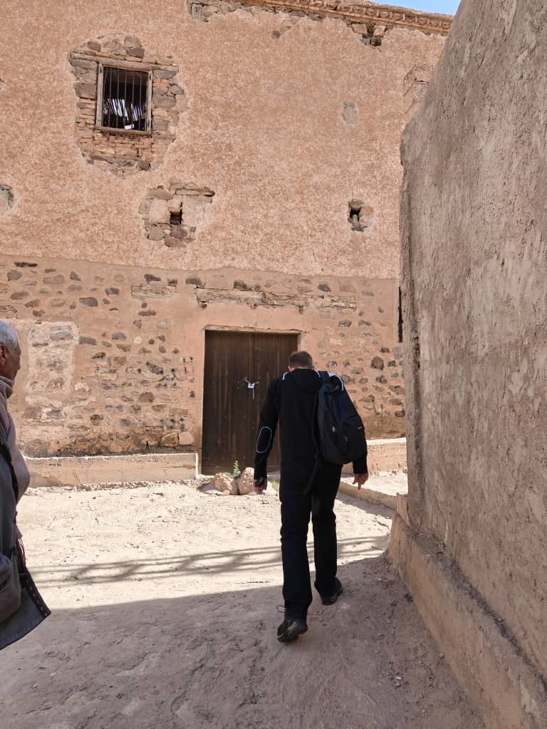 A traveller walking a narrow earthen lane between the mud-rendered walls of a ksar