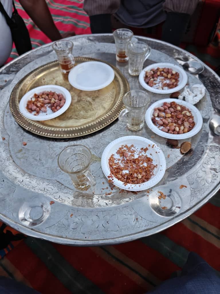 A silver tray of tea glasses and roasted peanuts at a desert camp