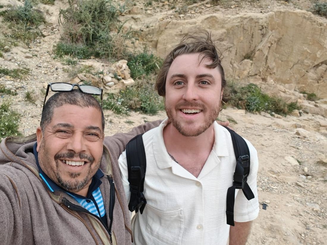An Algerian guide and a traveller laughing together on a stony hillside