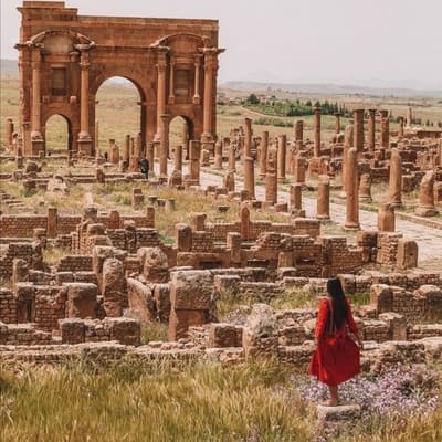 The Arch of Trajan and the colonnaded streets of Timgad, a visitor walking among spring flowers