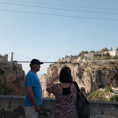 Two travellers at a viewpoint above the Rhumel gorge, the Sidi M'Cid suspension bridge strung across it behind them