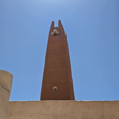 The plain ochre minaret of a M'Zab mosque rising into a deep blue sky, its four finials against the sun