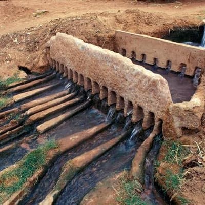 A foggara water divider in the Gourara, its comb of openings splitting the flow between garden channels