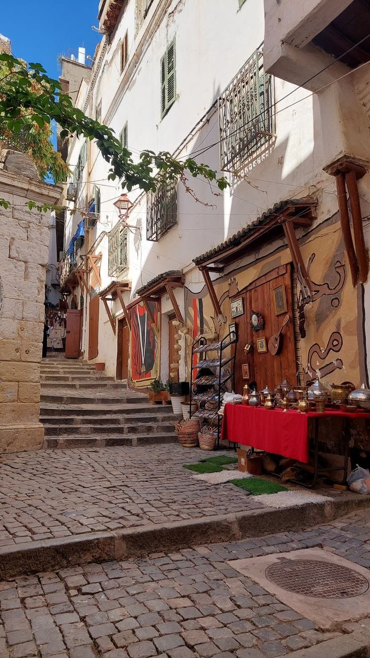 A stepped cobbled lane in the Casbah of Algiers, brass and copperware laid out at a doorway