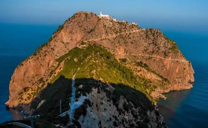 A lighthouse on the summit of a red rocky headland above the sea near Béjaïa