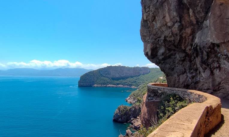 A cliffside road cut beneath an overhanging rock above the sea near Béjaïa