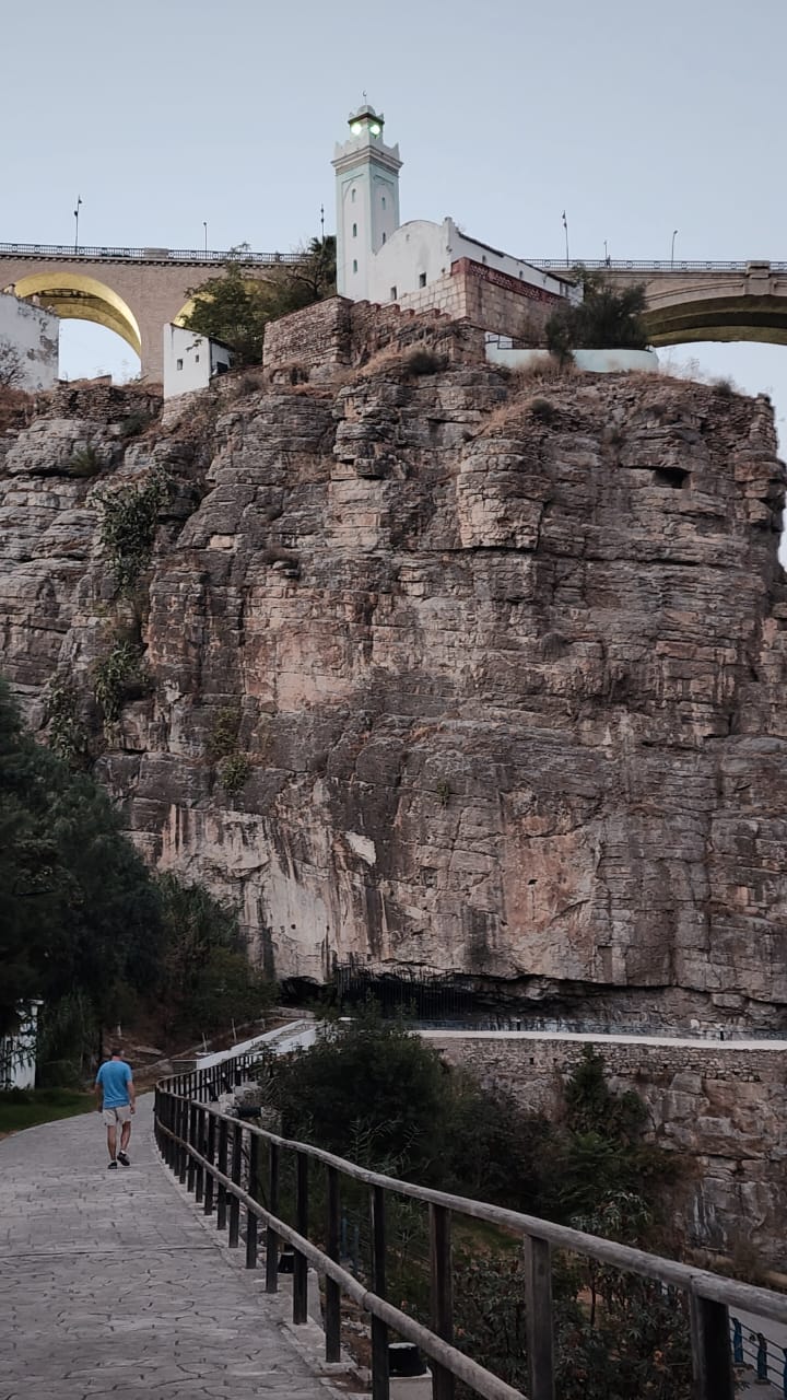 The walkway through the Rhumel gorge beneath Constantine's cliffs, a minaret and bridge arch on the rim above
