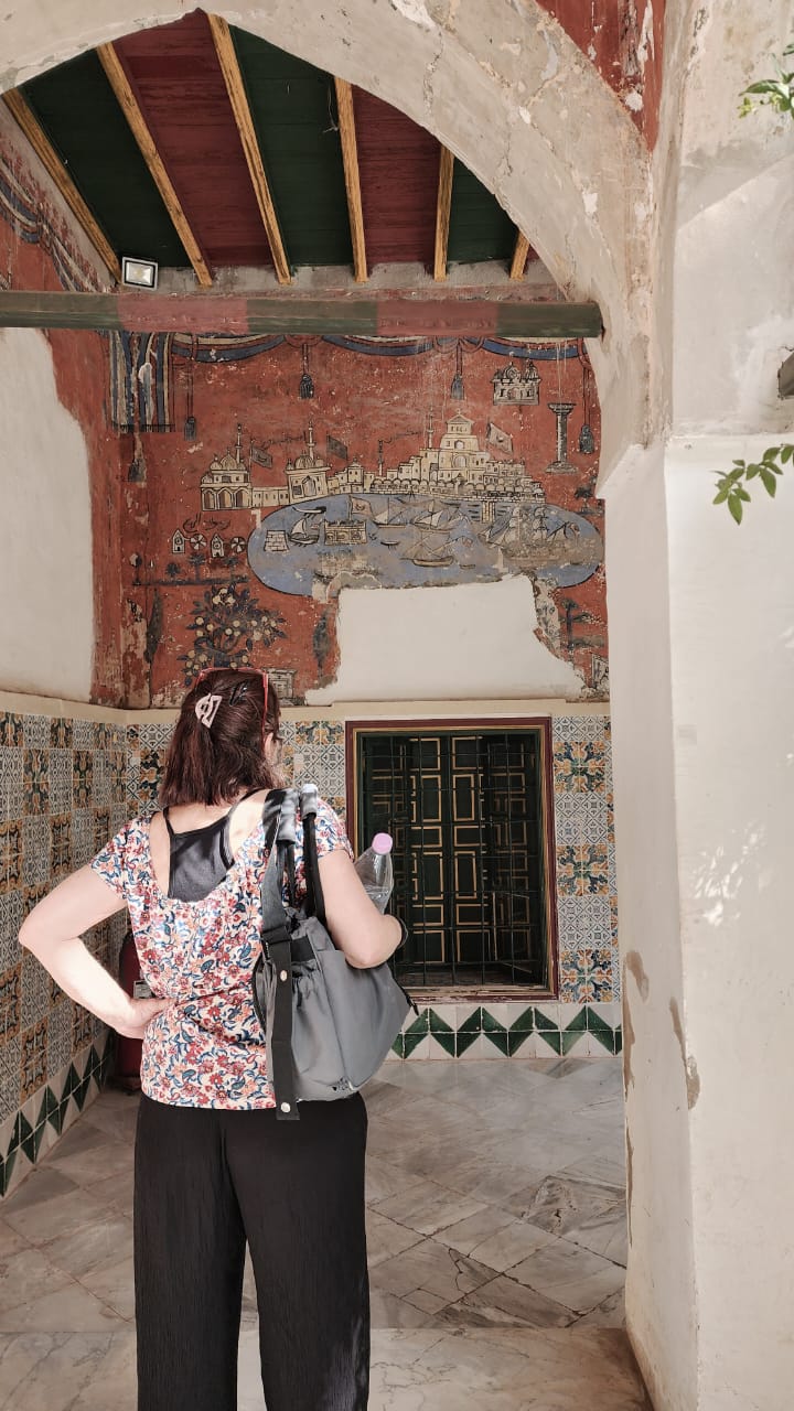 A naive wall painting of a harbour city above zellige tiling inside the Ahmed Bey Palace