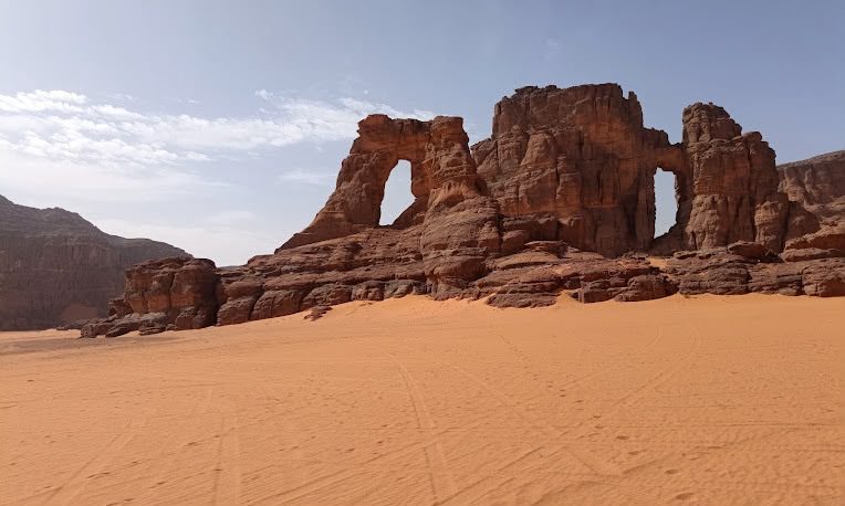 A natural sandstone arch rising above smooth orange sand in the desert around Djanet