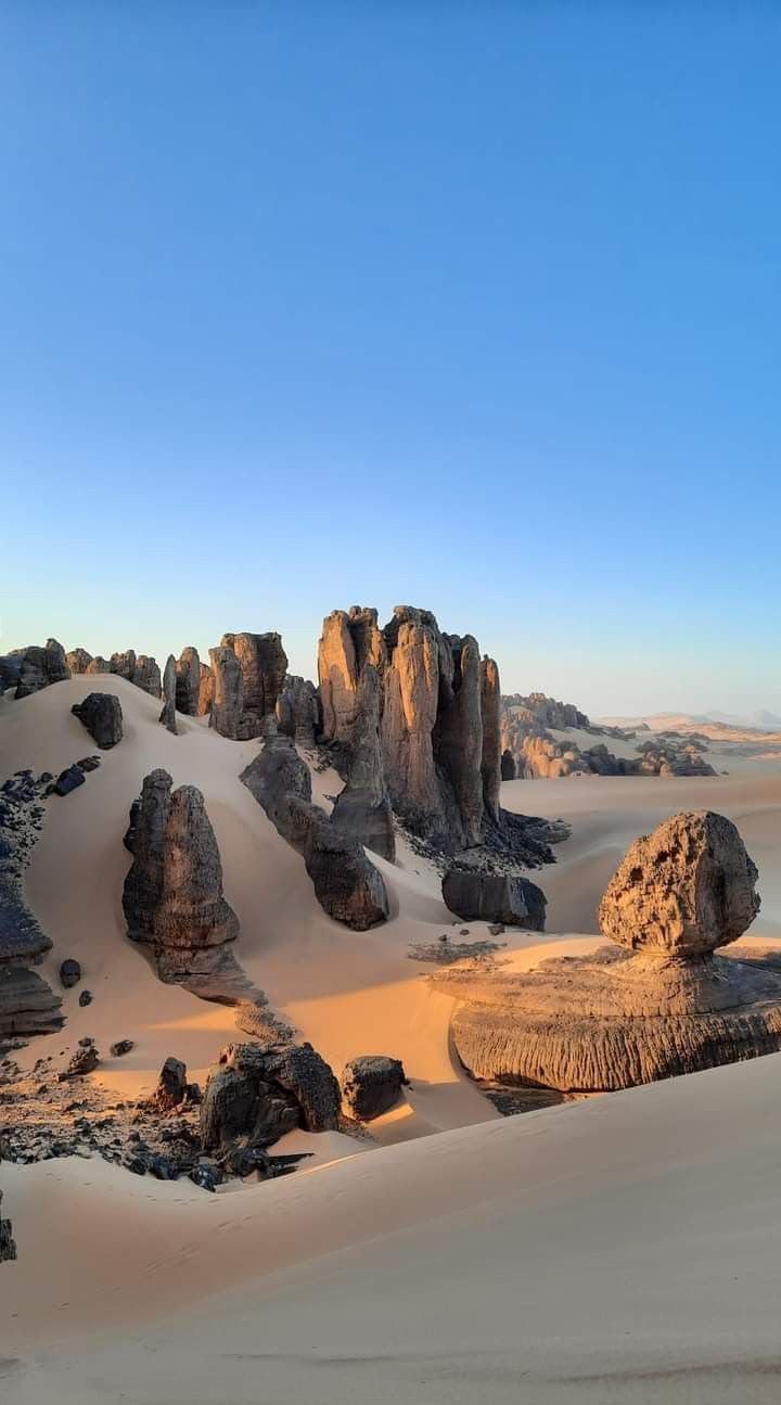 Rock towers and a mushroom-shaped boulder among pale dunes near Djanet