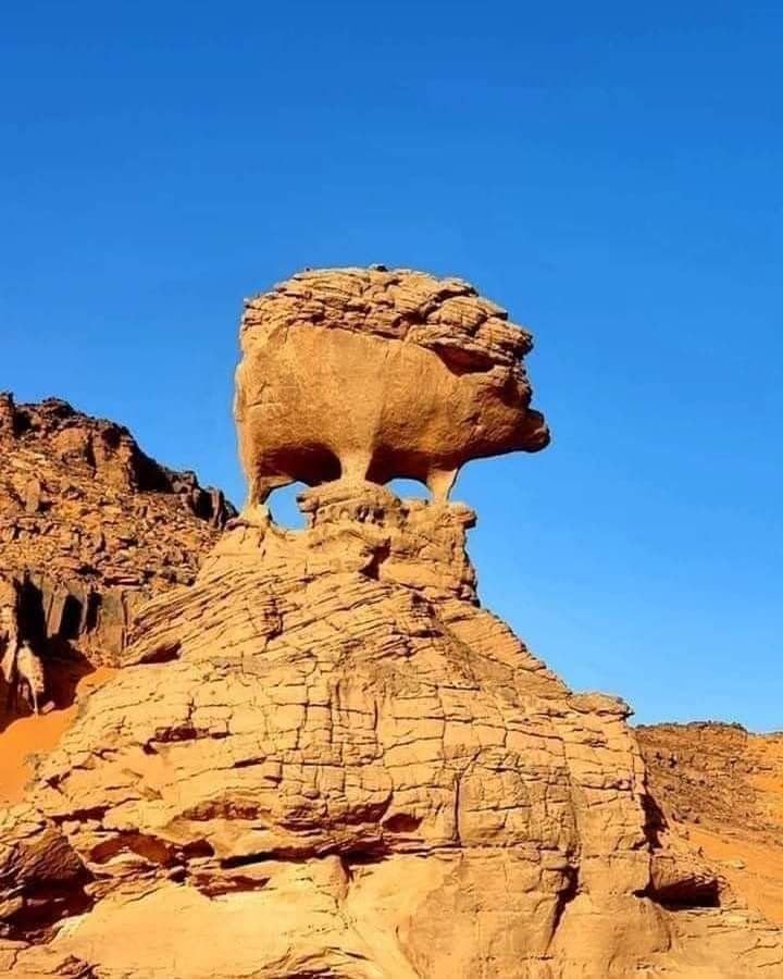 A sandstone boulder balanced on a narrow pedestal against a deep blue sky near Djanet