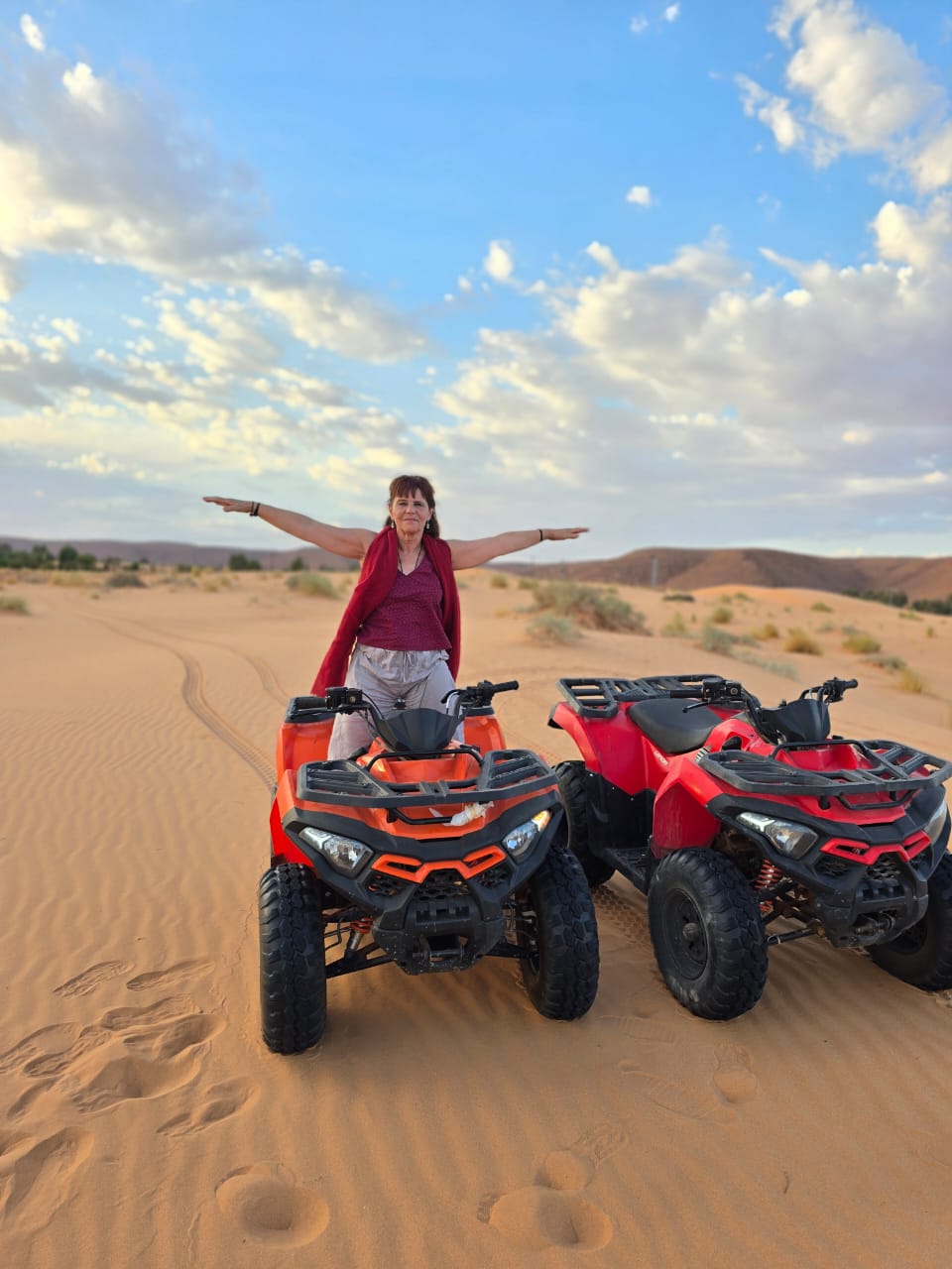 A traveller standing arms outstretched between two quad bikes on the sand at the end of the afternoon