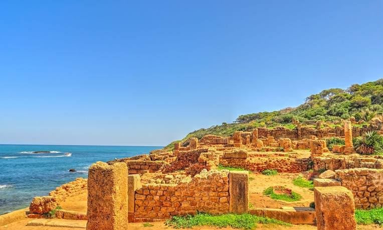 Low Roman walls on a grassy slope above the sea at Tipaza